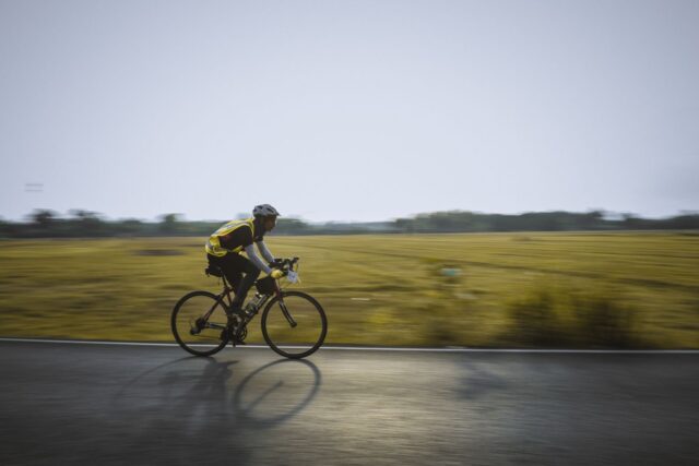 Biciclist cu cască și vestă reflectorizantă care pedalează pe o pistă de biciclete din oraș