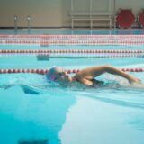 Adult care învață să înoate cu o placă de înot într-un bazin interior, alături de instructor