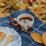 Persoană înfășurată într-o pătură care bea un ceai cald, cu pantofii de alergare lângă canapea