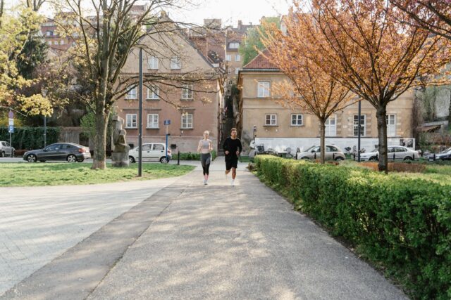 Doi prieteni care aleargă împreună pe o alee dintr-un parc, într-o dimineață de toamnă